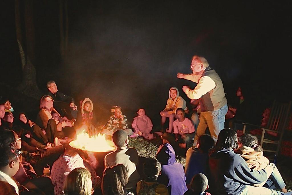 An old man telling a story around a campfire to kids
